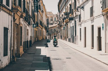 A young couple on motorbike between buildings on a sunny day in Cordoba, Spain