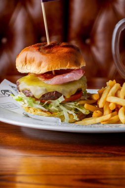 A vertical close-up shot of a cheeseburger with some french fries on a plate.