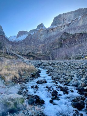 A mesmerizing view of beautiful snow-capped mountains with a small stream against a blue sky