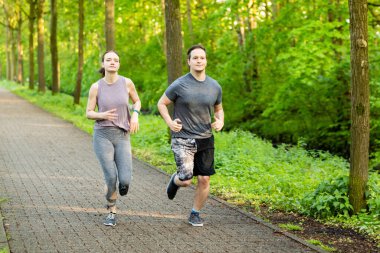 Genç bir kadın ve erkek ormanda koşuyor ve spor yapıyor.
