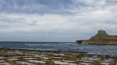 Salt pans of Gozo near the sea with a sea cave in view