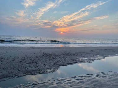 A scenic view of sea waves on a sandy beach against beautiful sky at sunset