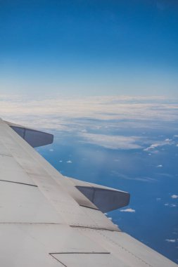 Mavi gökyüzü bulutlarına karşı yüksek irtifada uçan ticari uçağın kanadına bakın.