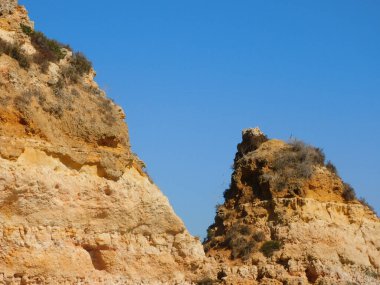 Mavi, berrak gökyüzünün altındaki taş tepelerin manzaralı bir görüntüsü.