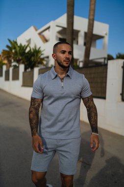 Aynı tişörtü ve şortu giyen dövmeli genç bir adamın dikey fotoğrafı.