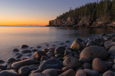 Acadia Ulusal Parkı 'nda yeşil tepeli ve turuncu gökyüzü olan güzel bir Boulder Sahili.