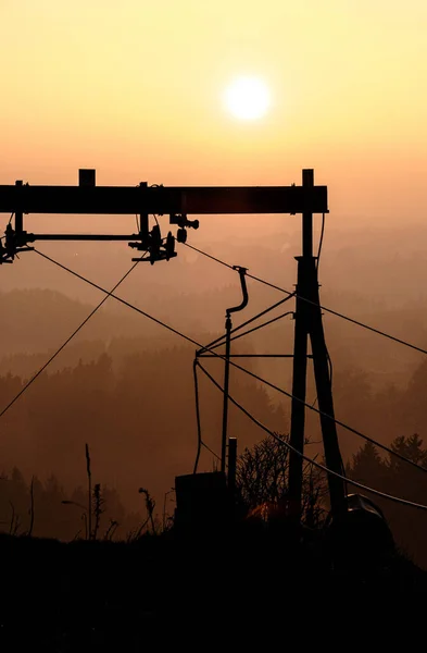 A vertical shot of the silhouettes of the industrial cables against the bright sunset.