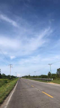 Uzun bir otobanın üzerinde beyaz bulutlar olan mavi bir gökyüzünün dikey görüntüsü