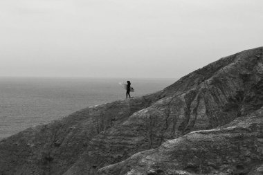 Kayalık bir dağda sörf yapan bir adamın gri ölçekli görüntüsü.