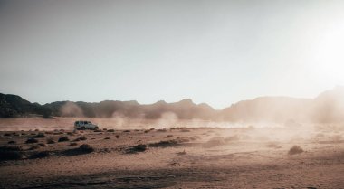 Güzel bir gün doğumunda çölde araba süren beyaz bir araba.