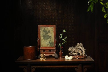 Küçük altın bir Buda heykeli ve seramik vazoda bir gül ahşap bir zeminde antik bir çerçeve. Karanlık bir arkaplan.