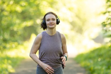 Kulaklıklı, ormanda koşan genç bir beyaz kadın.