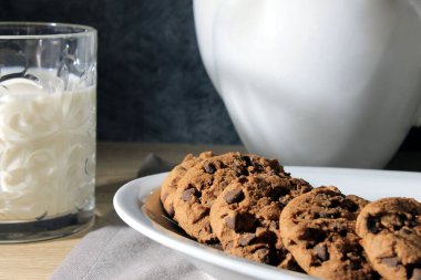 Çikolata parçalı kurabiyelerle kahvaltı, bir bardak süt, açık ahşap masa ve gri arka plan