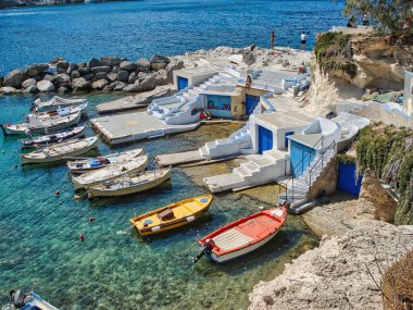 An aerial shot of small fishing boats by traditional homes in Milosis land, Greece and a blue sunny sky