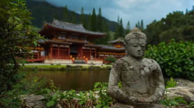 A statue against the Buddhist Temple Byodo-in surrounded by ponds and greenery at Auimanu, Hawaii