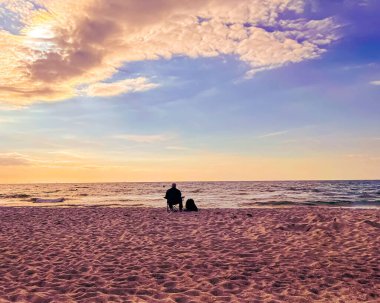 A scenic view of a person sitting on the beach during a bright sunset in the sky