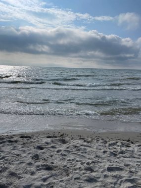 A vertical shot of sea waves on a sandy beach against beautiful clouds