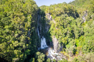 A bird's eye view of a waterfall flowing down the mountains covered with greenery in New Zealand
