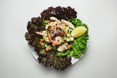 Marullu karides salatası ve beyaz bir masada beyaz bir tabakta bir dilim limon.