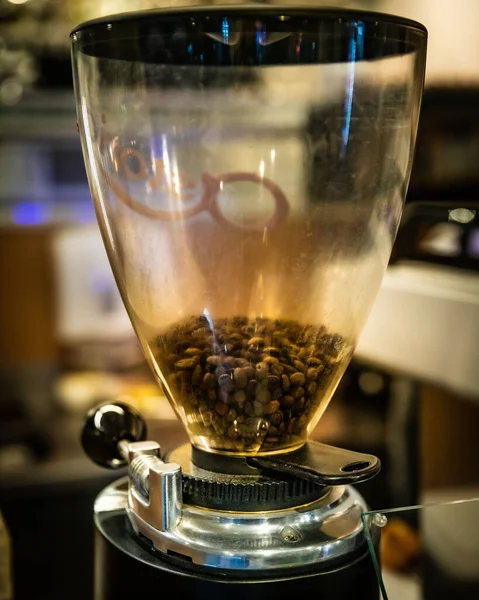 A vertical shot of a coffee grinder with coffee beans in it in the cafe