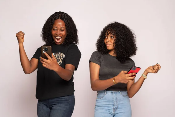 一张漂亮的照片拍到两个非洲女孩在检查她们的手机 一个很高兴 另一个则在孤独的背景下很伤心 — 图库照片