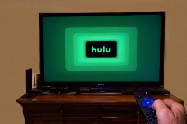 Hulu logosunu gösteren bir televizyonun önünde uzaktan kumandalı bir el.