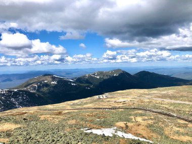Arka planda bulutlu gökyüzü olan dağlarda bir manzara.