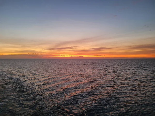 Mavi denizin üzerinde sakin dalgalarla manzaralı bir günbatımı.