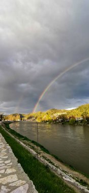 Kasvetli gökyüzünün dikey görüntüsü. Şehirde bir nehrin üzerinde gökkuşağı.
