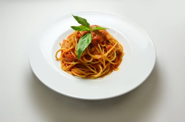 Beyaz bir masada beyaz bir tabakta soslu ve yeşillikli pişirilmiş spagetti.