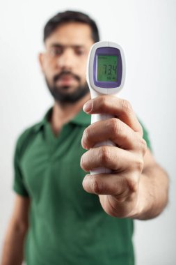 Indian guy showing his body temperature in a contactless digital infrared thermometer isolated in white background.