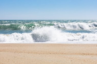 A beautiful landscape view of ebb and flow on a sandy beach with blue sunny sky on the horizon