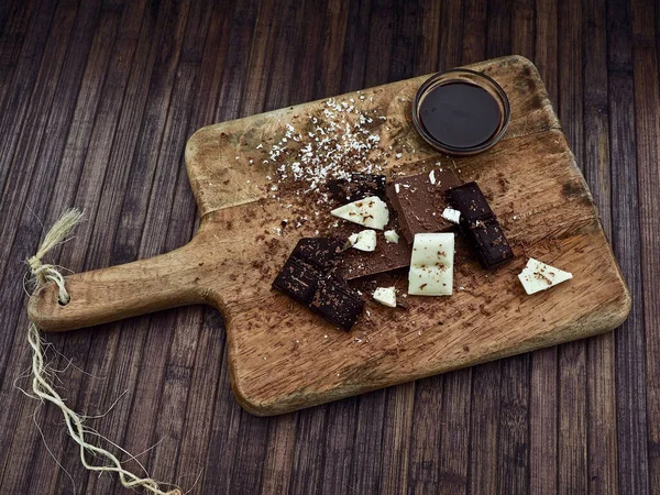 white, milk and dark chocolate, melted chocolate and chocolate shaves on a wooden tray, top view
