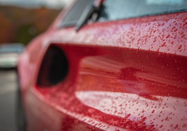 Kırmızı bir spor arabanın kenarındaki yağmur damlalarının yakın plan çekimi.