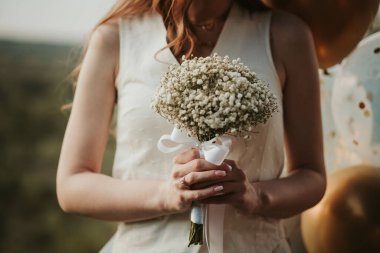 Gelinin düğün buketini çingene çiçekleriyle tutan ellerinin yakın çekimi.