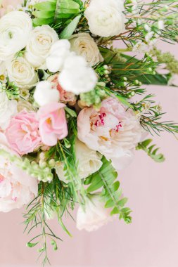 A vertical selective shot of a composition of white and pink roses and green branches on a light background