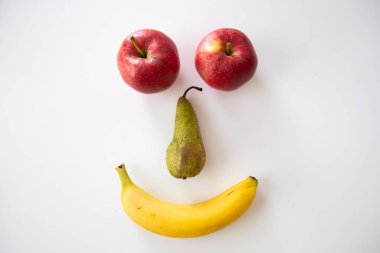 A smiley face made with banana, apple and pears on white background