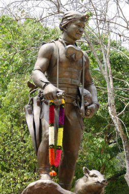 A vertical shot of an old man statue in a rural area with trees in the background