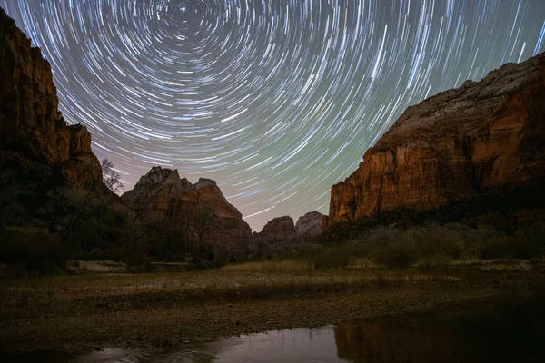 The sky with a trail of circumpolar stars revolving on the polar star with the natural rocky landscape