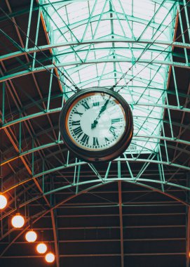 A vertical low angle shot of a clock hanging from a metal ceiling in a train station