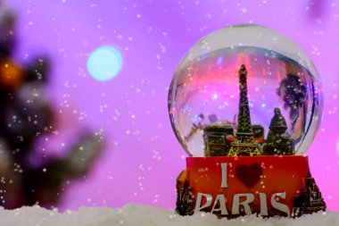 A closeup shot of the snowflakes falling over a Paris Eiffel Tower Snow Globe Souvenir on a blurred purple background