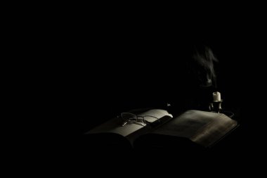 A book and glasses next to a candle with smoke on a dark background