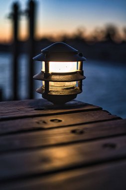 Gün batımının bulanık arka planına sahip ahşap bir masanın üzerindeki bir lambanın sığ odağı