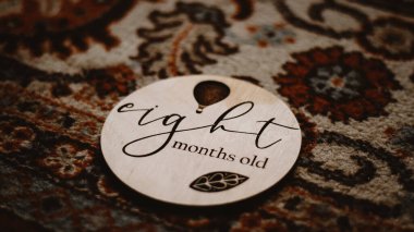 A closeup of the engraved plywood tag of an eight-month-old baby sign on the carpet. Selected focus.