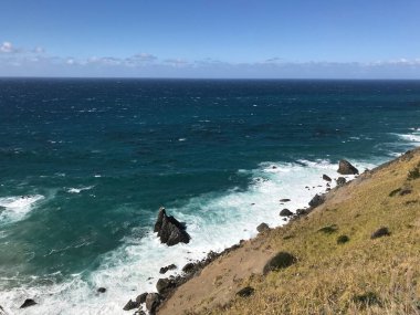 Güneşli bir günde kıyı manzarası ve deniz dalgalarının yüksek açılı görüntüsü.