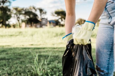 Gezegenimize bakan kişi ekosistemden çöp topluyor, kot pantolon, beyaz gömlek ve sarı eldiven giyiyor..