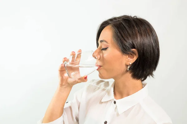 A closeup of a young Latin American woman drinking water from a glass on a white background