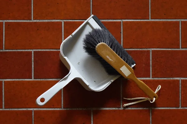12 March 2022, Dahlbruch, NRW, Germany, Wooden hand sweep and grey plastic dustpan on dusty dark red tile floor, concept: cleaning, household