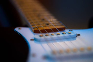 A selective focus shot of the top pick-up of white electric guitar in the dark