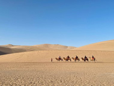 A caravan of camels and people walking in a desert with clear sky background